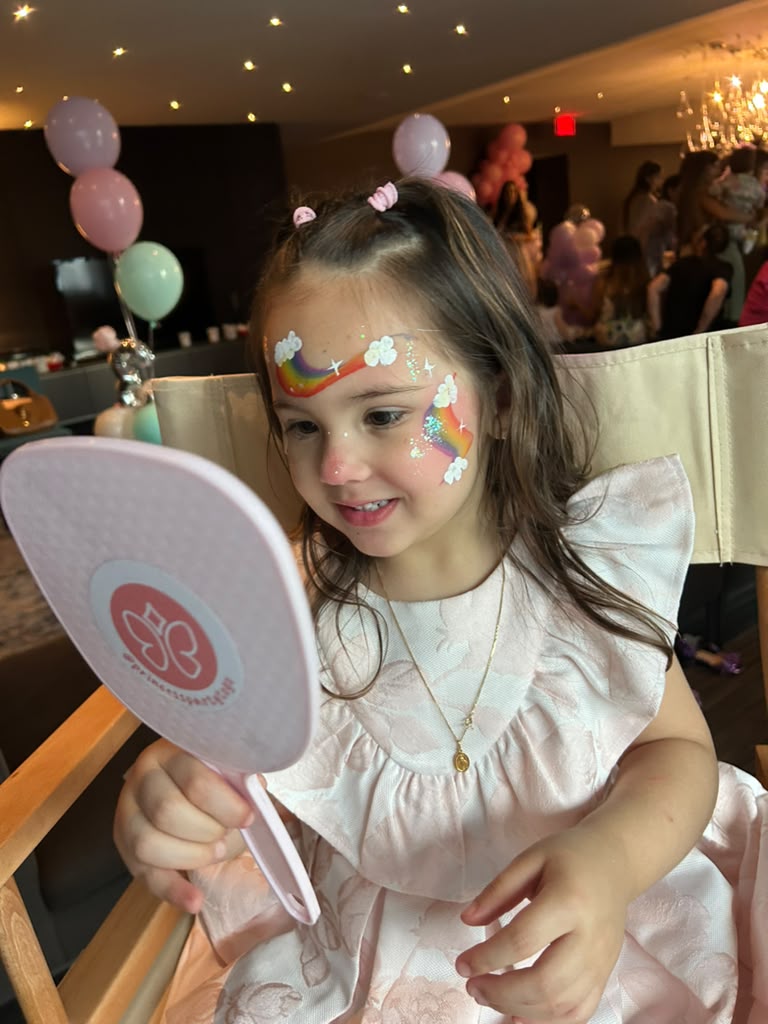 Girl admiring her rainbow face painting in the mirror