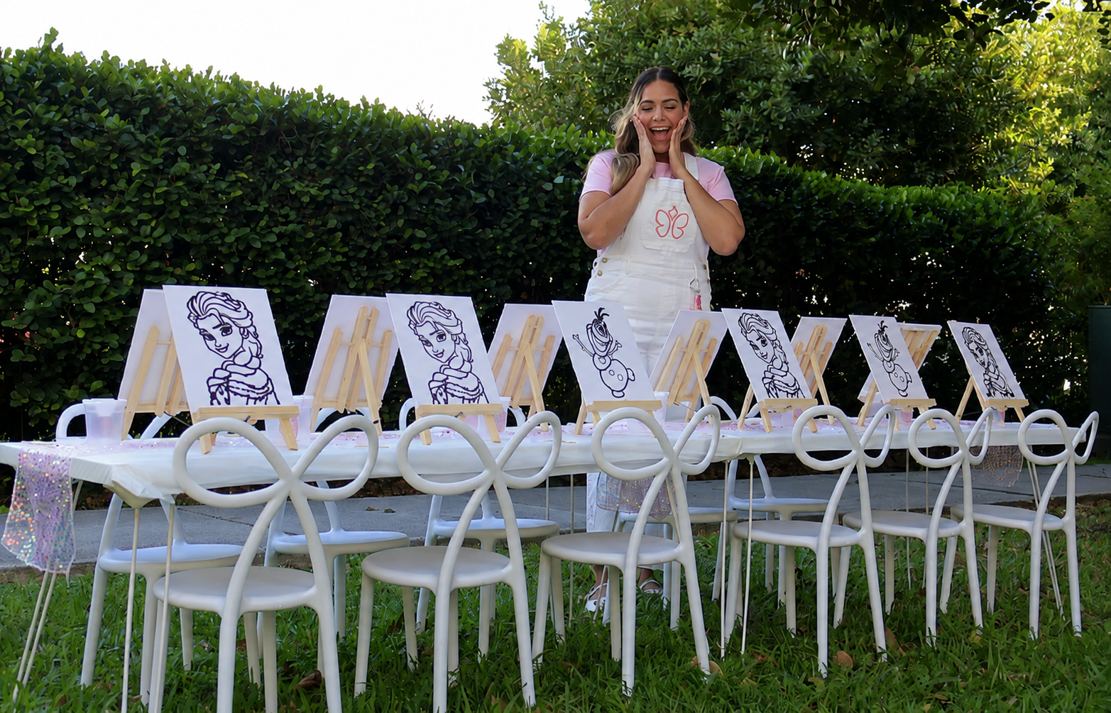 A cheerful host standing behind a craft table with painting easels for a kids party