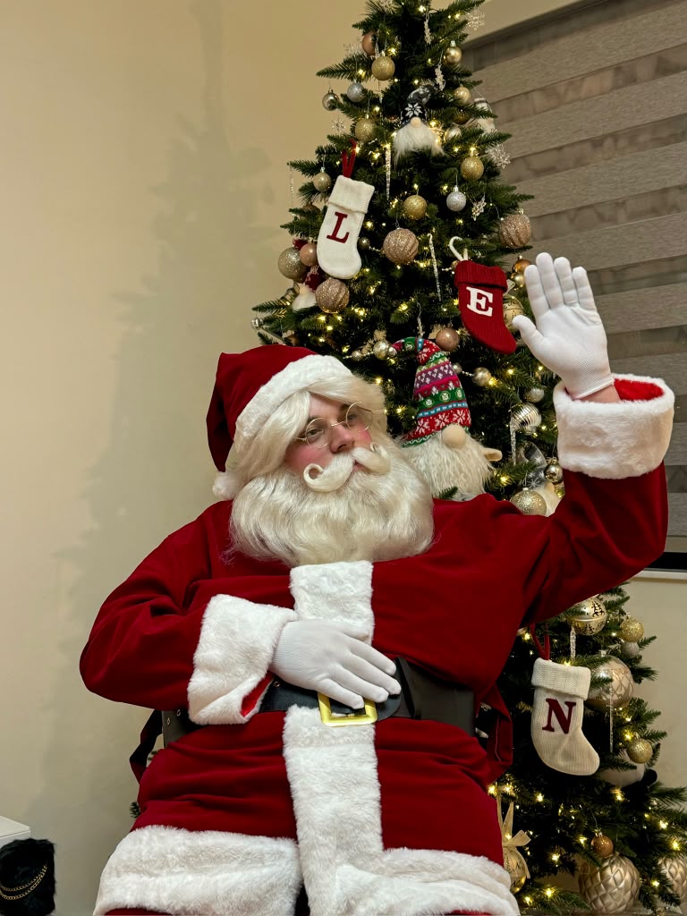 Santa Claus waving beside a decorated Christmas tree