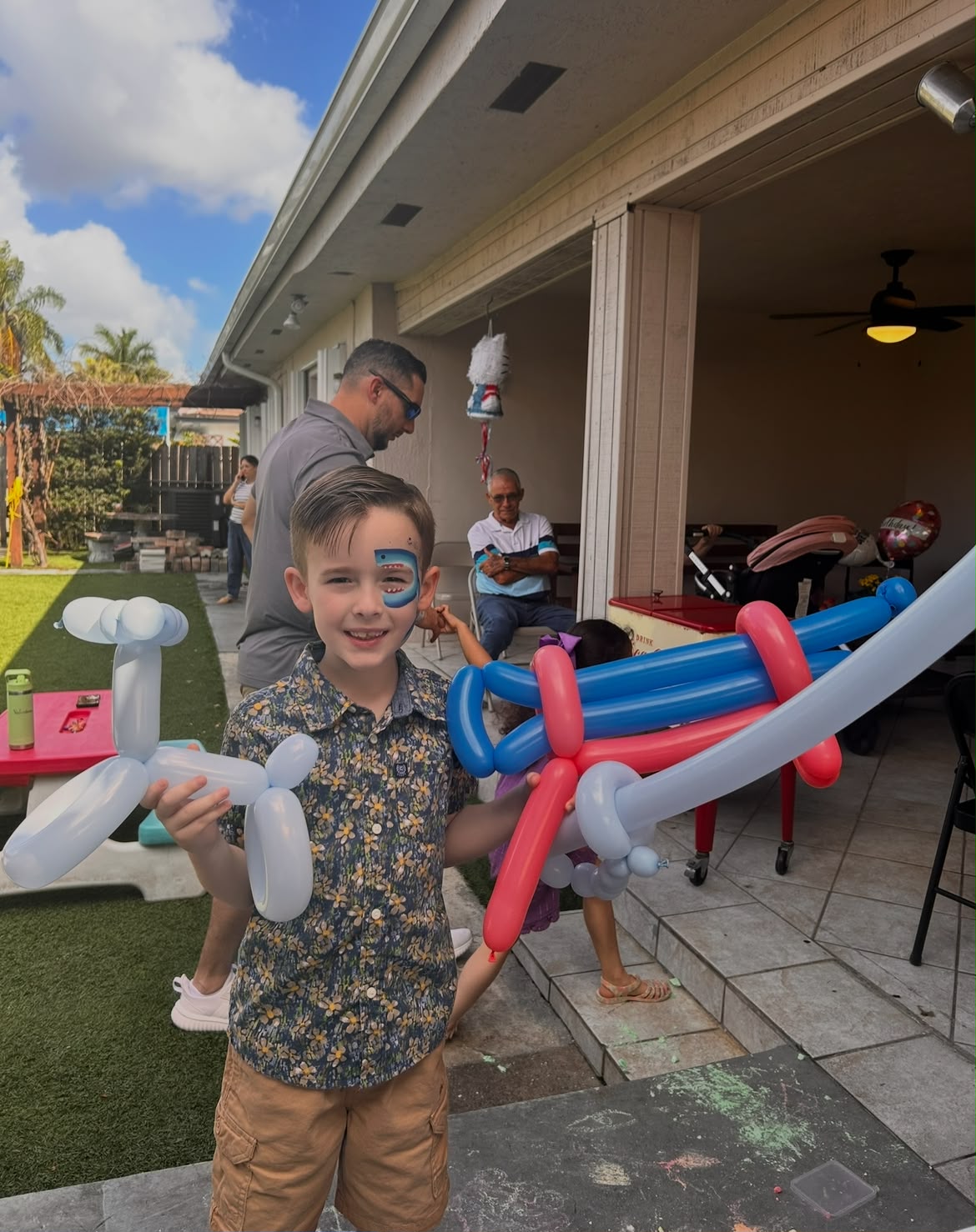 Boy with a shark face painting holding balloon art at an outdoor party