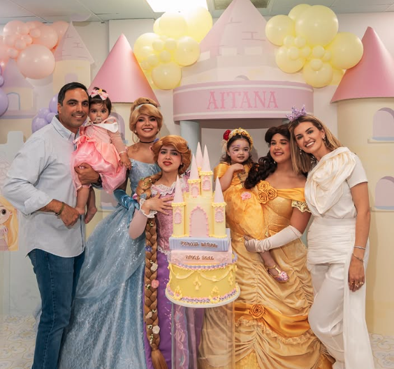 Family celebrating with princess characters beside a castle birthday cake