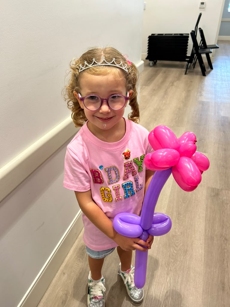 Birthday girl in a tiara holding a large balloon flower