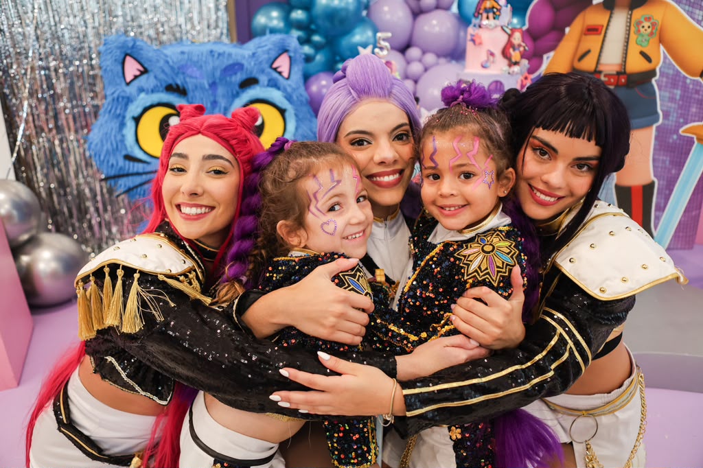 Pop-star characters hugging two face-painted girls at a themed celebration